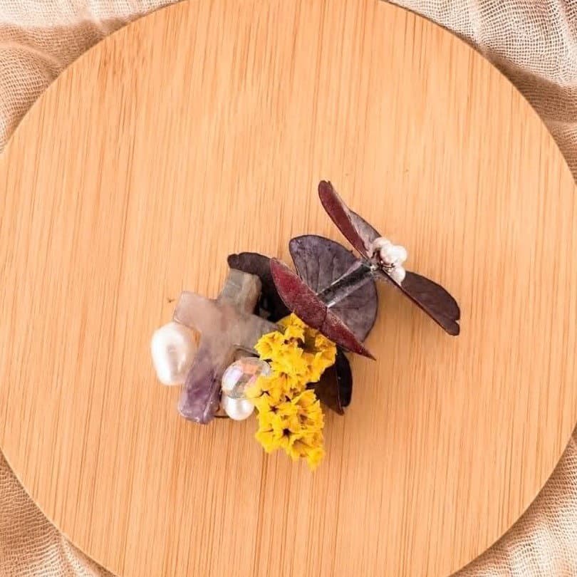 broche décorative avec fleurs séchées jaunes, feuilles violettes et perles blanches sur support en bois clair